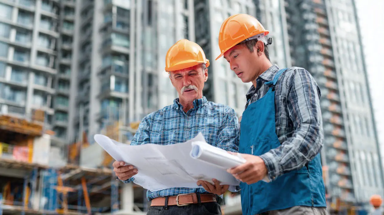 Two construction professionals reviewing drawings together at a high-rise building site